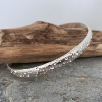 Image of a unique patterned silver bangle. The random pattern looks like lots of different sized bubbles