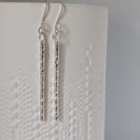 Image of a pair of silver stick earrings with a heavy sparkly pattern.