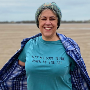 A woman wearing a seafoam green t-shirt, hat and checked jacket.