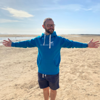 A man wearing a tropical blue hoodie with his arms outstretched.