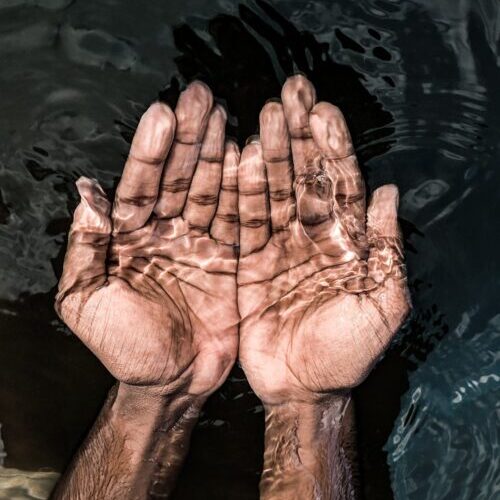 From above of crop anonymous male washing hands in clean water of lake in daytime