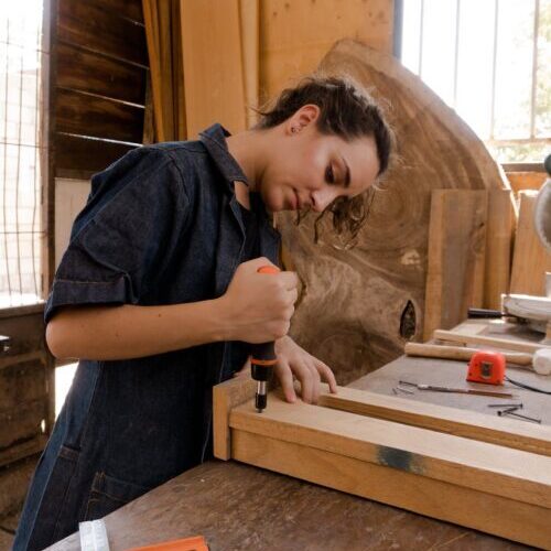 Woman in Blue Coveralls Using a Carpentry Tool 