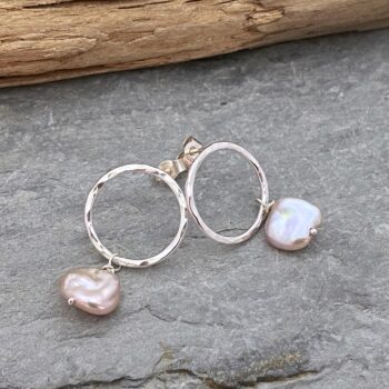 Image of a pair of sterling silver open circle stud earrings each with a unique pink keshi pearl dangling from the bottom of the circle