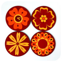 Set of four 70s style flower coasters in oranges, yellows and browns on a white background